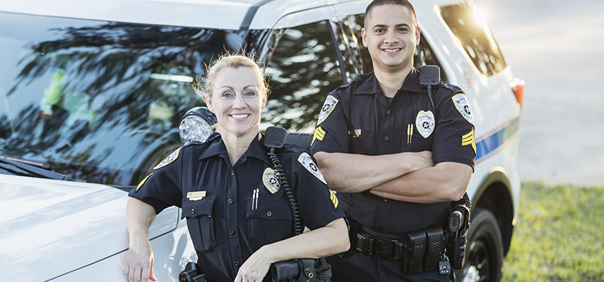 A female police officer and her male partner stand next to their squad car